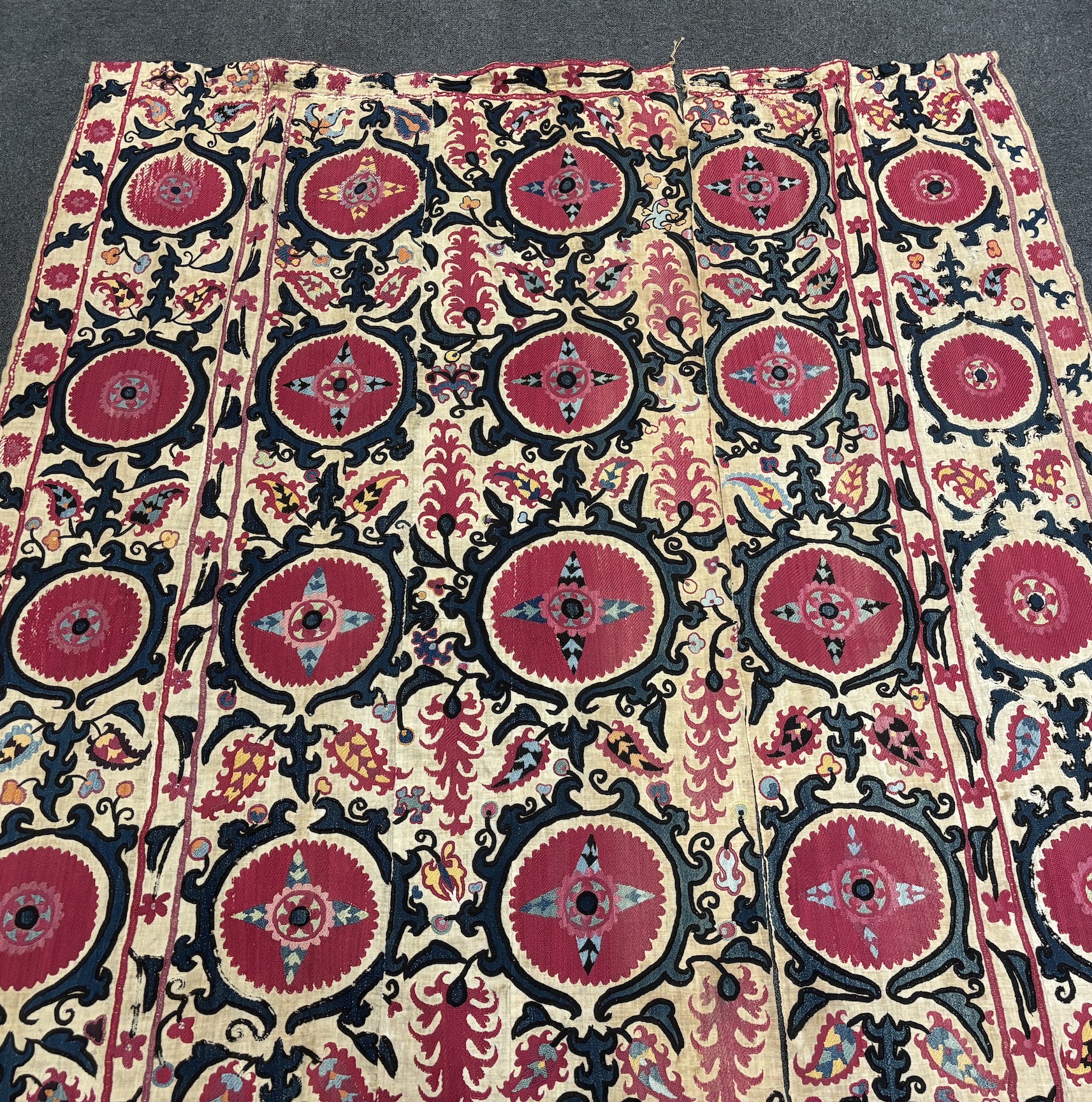 An 19th century Uzbek Suzani embroidered wall hanging, in two pieces, the main hanging sewn together as four panels, together with a fifth matching border, being detached, embroidered with large bold floral motifs, in ri